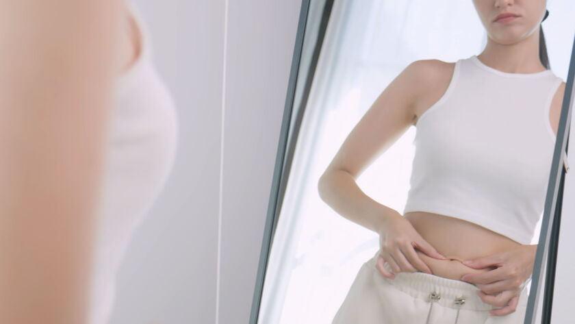 A young woman is worried about her body while looking in the mirror image