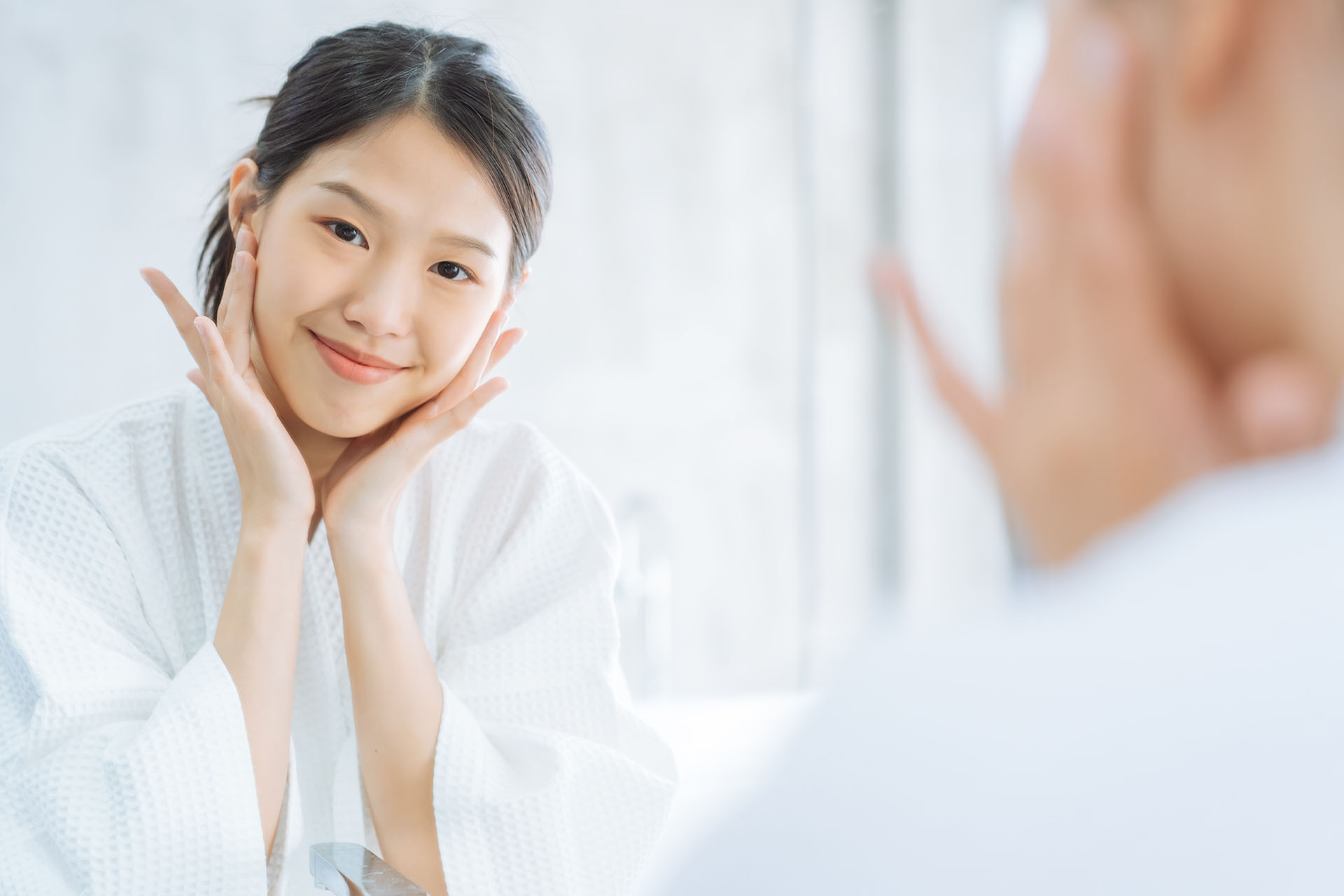 Female Skin Care. Young asian woman touching her face and looking to mirror in bathroom image
